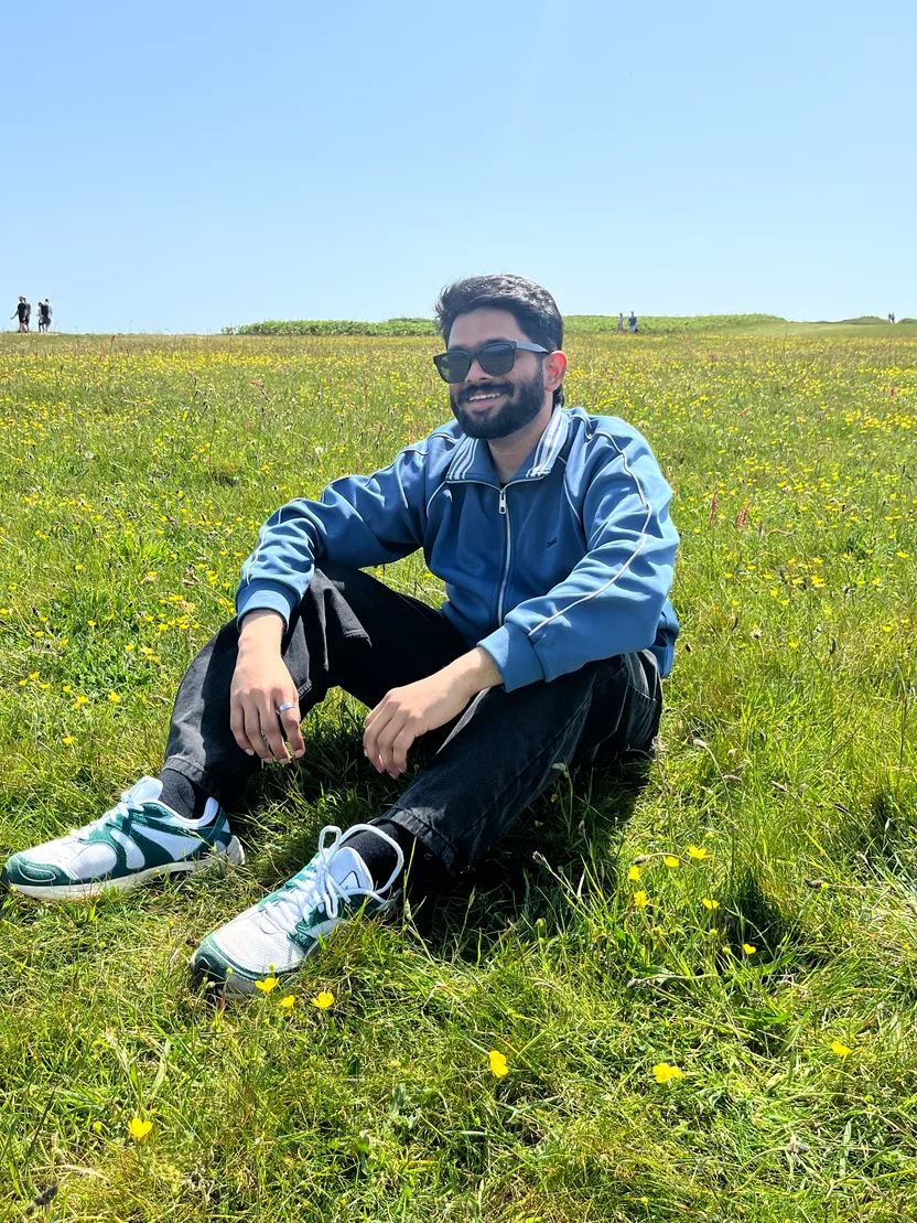 Rahul sitting in a sunlit meadow of buttercups under a clear blue sky